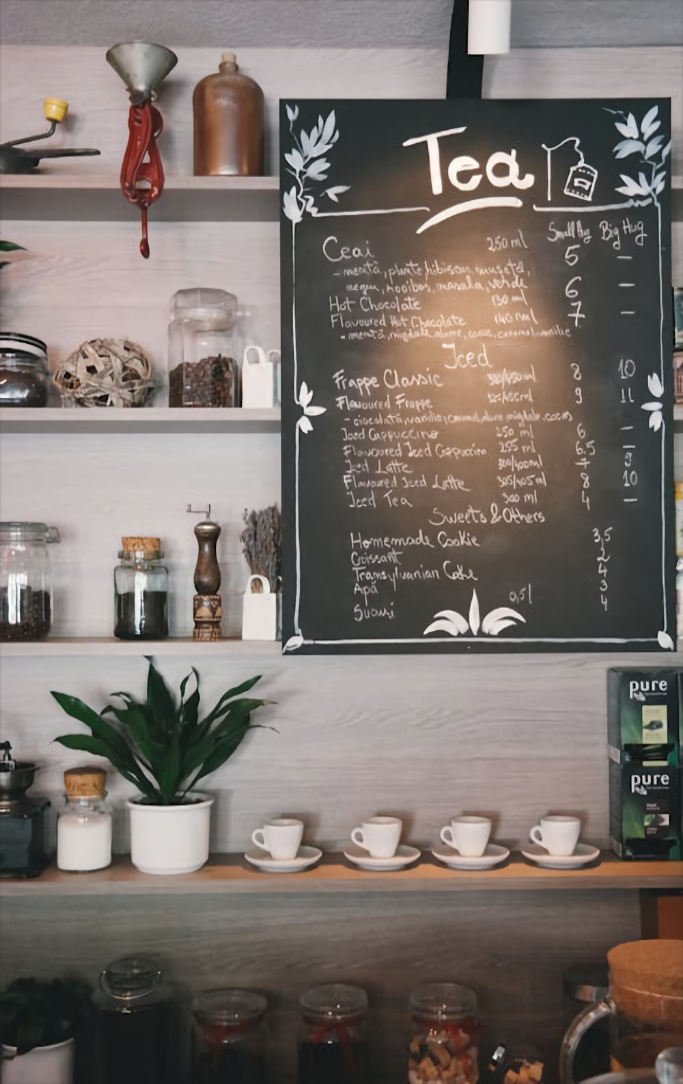 A cafe with a menu board showing tea choices with shelves of tea and cups below