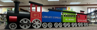 A full-width view of the child size train in the library. The wording on the side of the train reads Library Express All Aboard